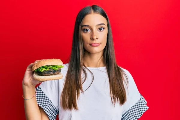 Young Hispanic Woman Eating Hamburger Thinking Attitude Sober Expression Looking — Stock Photo, Image