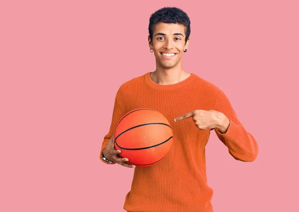 Молодой Афроамериканец Держащий Баскетбольный Мяч Улыбается Показывая Пальцем Рукой — стоковое фото