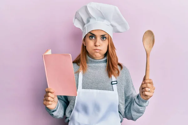 Hispanic Young Chef Woman Reading Recipes Book Puffing Cheeks Funny — Stock Photo, Image