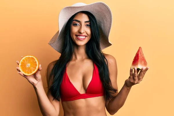 顔に幸せとクールな笑顔でスイカとオレンジの笑顔を食べる美しいヒスパニック系の女性 歯を見せて — ストック写真