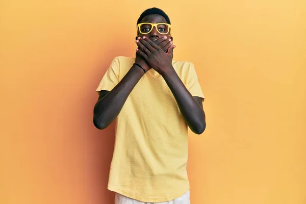 カジュアルな服と眼鏡を身に着けている若いアフリカ系アメリカ人の男性は間違いのために手で口をカバーショックを受けた 秘密の概念 — ストック写真