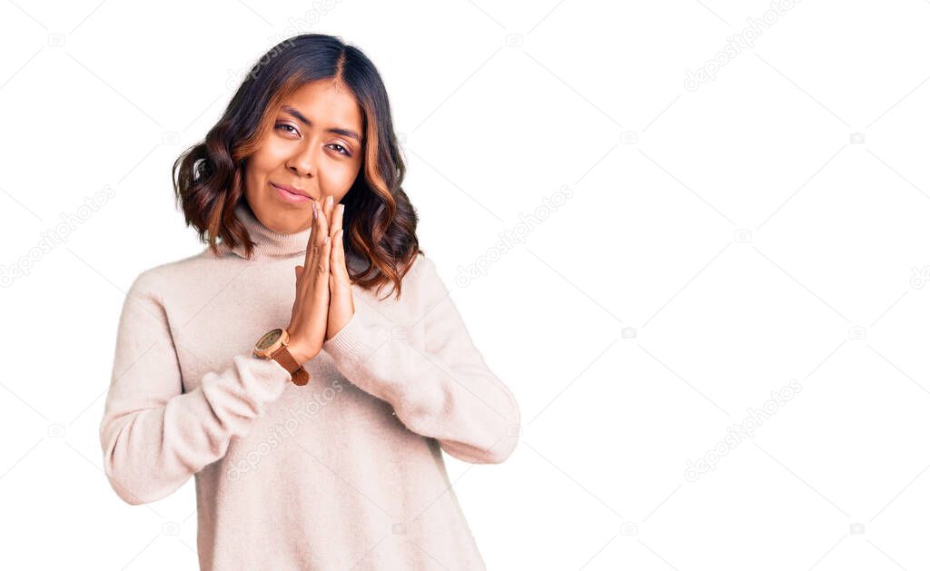 Young beautiful mixed race woman wearing winter turtleneck sweater praying with hands together asking for forgiveness smiling confident. 