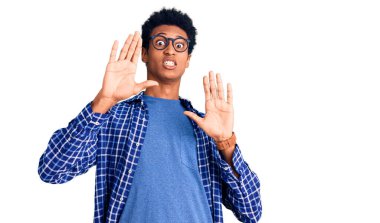 Sıradan kıyafetler ve gözlük takan, korku ifadesinden korkan genç Afrikalı Amerikalı adam. El hareketlerini durdur, şok içinde bağır. panik konsepti. 