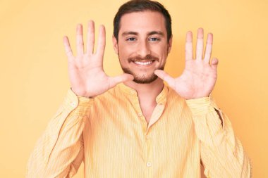 Gündelik kıyafetler giyen genç ve yakışıklı bir adam dokuz numarayı gösterip işaret ederken kendinden emin ve mutlu bir şekilde gülümsüyor.. 