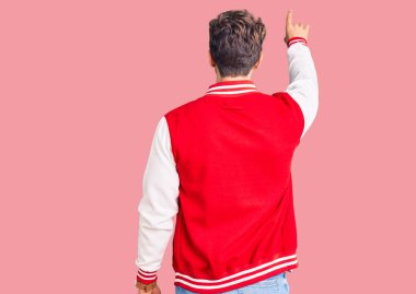 Beyzbol üniforması giyen genç yakışıklı adam geriye doğru poz veriyor. 