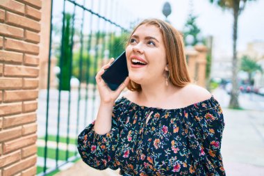 Genç kızıl saçlı kadın şehrin caddesinde akıllı telefondan konuşuyor..
