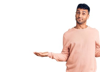 Gündelik kıyafetler giyen genç İspanyol adam gülümseyerek iki elini de açık tutuyor, sunuyor ve reklam karşılaştırması yapıyor ve dengeyi sağlıyor. 