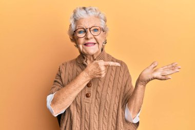Yaşlı, gri saçlı, günlük kıyafetler ve gözlük takan kadın kameraya hayret ediyor ve gülümsüyor.. 