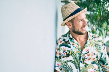 Yazlık şapkalı ve çiçekli tişörtlü yakışıklı beyaz adam dışarıda mutlu gülümsüyor.