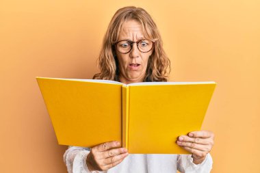 Orta yaşlı sarışın bir kadın kitap okuyor. Gözlük takıyor. Şaşırmış ve şaşırmış bir ifade, korku ve heyecanlı bir yüz ifadesi var.. 