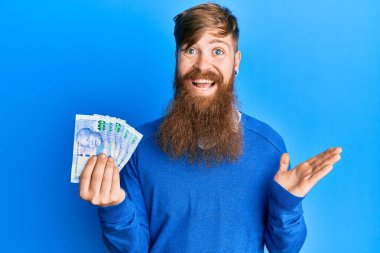 Genç İrlandalı kızıl saçlı adam Güney Afrika 'yı elinde tutuyor. 100 rand banknot başarıyı mutlu bir gülümsemeyle kutluyor ve kazanan el kaldırarak ifade ediyor. 