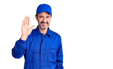 Middle age handsome man wearing mechanic uniform waiving saying hello happy and smiling, friendly welcome gesture 