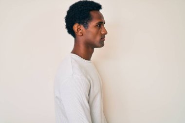 Kış süveteri giyen Afrikalı yakışıklı bir adam, rahat profil pozu veriyor, doğal bir yüzü ve kendine güvenen bir gülümsemesi var.. 