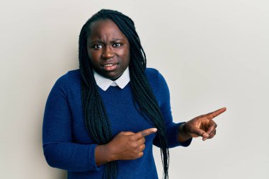 Saçları örgülü genç siyahi bir kadın parmaklarını yana doğru uzatıyor ve kafası karışık bir ifade takınıyor. şüphe kavramı. 