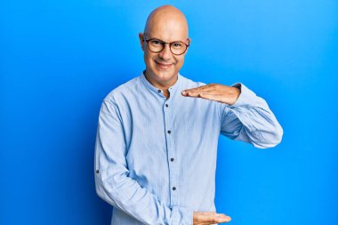 Orta yaşlı, kel, sıradan kıyafetler giyen ve elleri büyük ve büyük bir işaret gösteren gözlüklü bir adam. Ölçü sembolü. Kameraya bakıp gülümsüyor. ölçüm kavramı. 