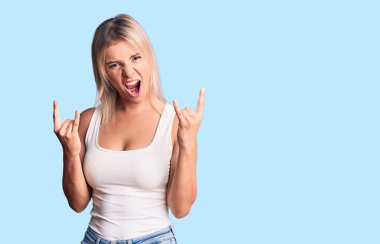 Kolsuz tişört giyen, çılgın bir ifadeyle bağıran genç, güzel sarışın kadın elleri havada rock sembolü yapıyor. Müzik yıldızı. ağır kavram. 