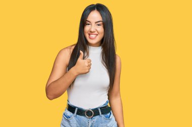 Gündelik kıyafetler giyen genç, güzel İspanyol kız elinle mutlu bir jest yapıyor. Kameraya bakıp başarıyı gösteren ifade. 