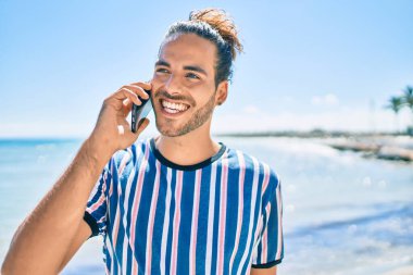 Genç İspanyol gülümseyen adam sahilde akıllı telefondan konuşarak mutlu oluyor..
