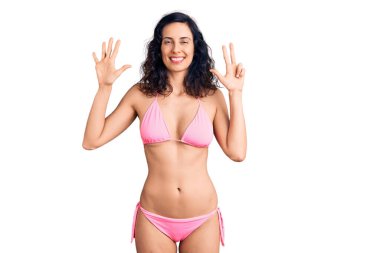 Genç ve güzel İspanyol kadın bikini giyiyor ve 8 numaralı parmaklarıyla işaret ederken kendinden emin ve mutlu gülümsüyor.. 
