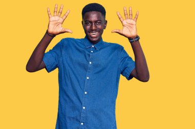 Genç Afro-Amerikalı günlük giysiler giymiş on numarayı gösterip işaret ederken kendinden emin ve mutlu bir şekilde gülümsüyor.. 