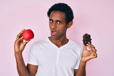 Şok olmuş yüzünde kırmızı elmalı ve çikolatalı waffle tutan yakışıklı bir Afrikalı. Şüpheci ve alaycı görünüyor. 