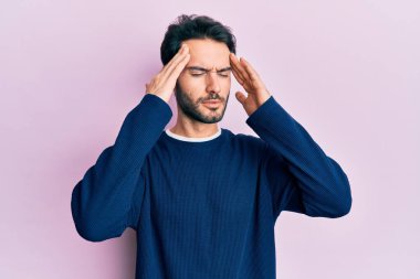 Latin asıllı genç bir adam elleri kafasında günlük kıyafetler giyiyor, stres yüzünden baş ağrısı çekiyor. migren ağrısı. 