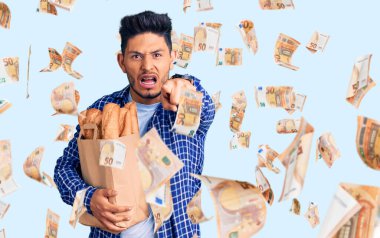 Yakışıklı Latin Amerikalı genç adam elinde bir kese kağıdıyla kameraya kızgın ve sinirli bir şekilde ekmek gösteriyor.