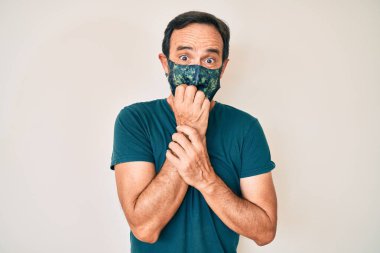 Orta yaşlı İspanyol bir adam kovid 19 koruma maskesi takıyor. Ağzı tırnak yiyen elleri yüzünden gergin ve stresli görünüyor. anksiyete. 