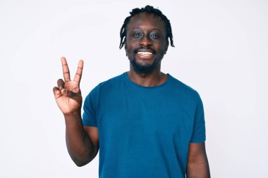 Saçları örgülü genç Afro-Amerikalı adam iki numarayı gösterip gösterirken kendinden emin ve mutlu bir şekilde gülümsüyor.. 