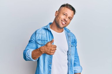 Sıradan kot ceket giyen yakışıklı kaslı adam elinle mutlu bir jest yapıyor. Kameraya bakıp başarıyı gösteren ifade. 