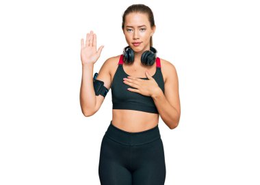 Güzel sarışın kadın spor kıyafetleri giyiyor ve kulaklık takıyor. Göğüs ve avuç içi açık küfürler ediyor. Sadakat yemini ediyor. 