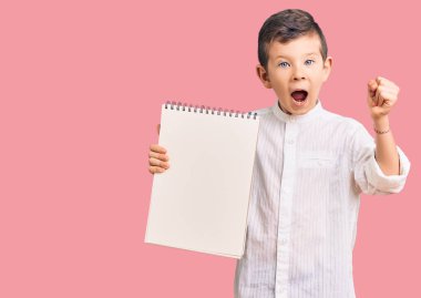 Sevimli sarışın çocuk elinde defterle gururla bağırıyor zaferi ve başarıyı kutluyor. Kollarını kaldırıp heyecanla bekliyor. 