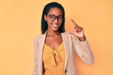 Genç Afro-Amerikan kadın iş kıyafetleri içinde gülümseyen ve el hareketleriyle hareket eden parmaklarıyla işaret yapan ve kameraya bakan. ölçüm kavramı. 