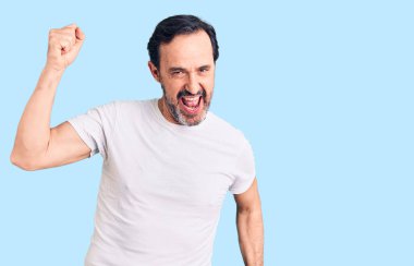 Orta yaşlı yakışıklı adam gündelik tişört giyiyor mutlu ve neşeli dans ediyor, gülümsüyor rahat ve kendinden emin bir şekilde müzik dinliyor. 