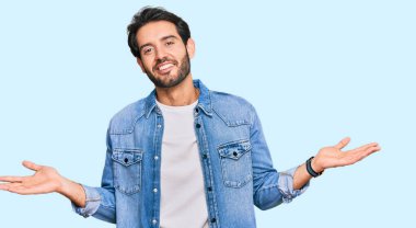 Gündelik kıyafetler giyen genç İspanyol adam gülümseyerek iki elini de açık tutuyor, sunuyor ve reklam karşılaştırması yapıyor ve dengeyi sağlıyor. 