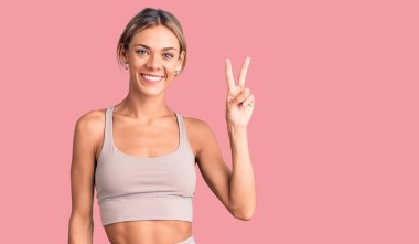 Güzel beyaz kadın spor giysisi giyer ve iki numarayı göstererek gülümserken kendinden emin ve mutlu.. 