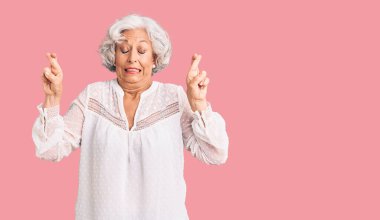 Üstün gri saçlı, sıradan kıyafetler giyen, umut dolu ve gözleri kapalı bir şekilde parmaklarını çapraz gösteren yaşlı bir kadın. Şans ve batıl inançlar. 