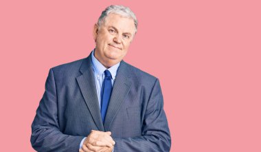 Yaşlı, gri saçlı, iş ceketi giyen, elleri birarada olan ve gülümseyen rahat ve neşeli bir adam. Başarı ve iyimserlik 