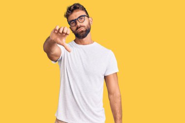 Gündelik kıyafetler giyen, gözlüklü, mutsuz görünen, reddedilmiş ve olumsuz davranan genç İspanyol bir adam. kötü ifade. 