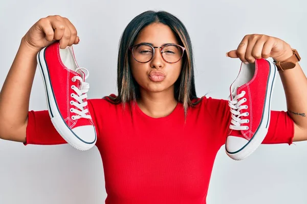 Joven Chica Latina Sosteniendo Zapatos Casuales Rojos Mirando Cámara Soplando —  Fotos de Stock