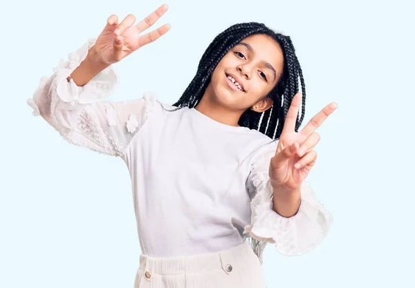 カジュアルな白いTシャツを着た可愛いアフリカ系アメリカ人の女の子が 勝利サインをしている指を見せてカメラを見て微笑んだ — ストック写真