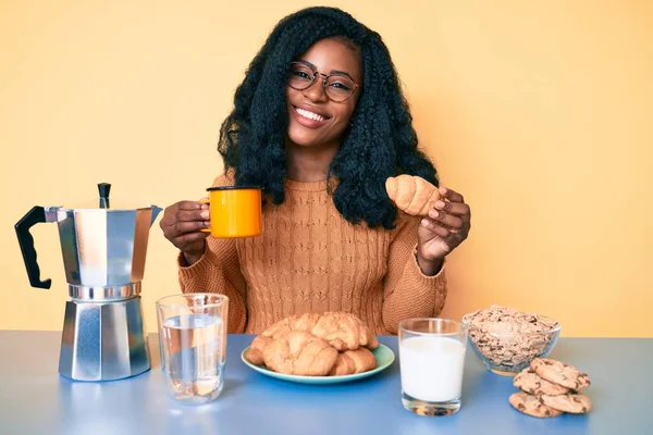 若いアフリカ系アメリカ人女性は 顔に幸せとクールな笑顔でクロワッサン笑顔を保持朝食を食べています 歯を見せて — ストック写真