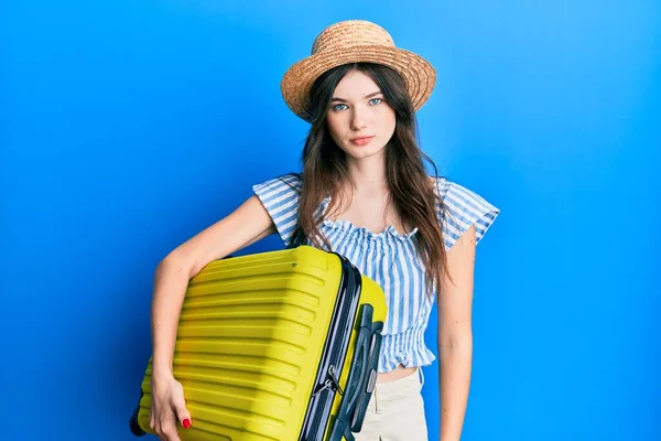 Young beautiful caucasian girl wearing summer dress and holding cabin bag thinking attitude and sober expression looking self confident