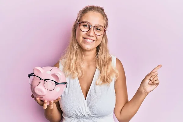 Jong Blond Meisje Holding Piggy Bank Met Bril Glimlachen Gelukkig — Stockfoto