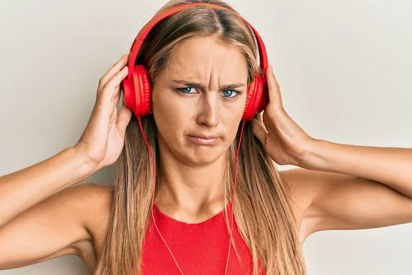 Jovem Loira Ouvindo Música Usando Fones Ouvido Cético Nervoso Franzindo — Fotografia de Stock