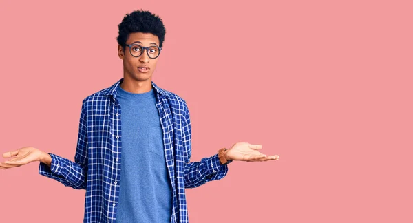 カジュアルな服と眼鏡を身に着けている若いアフリカ系アメリカ人の男性は 腕や手との混乱した表現を調達した 疑わしい概念 — ストック写真