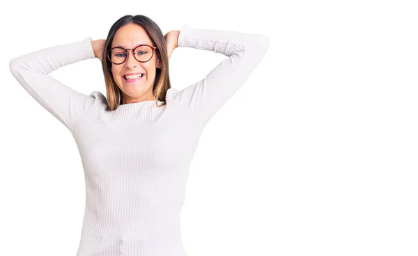 美しいブルネットの若い女性はカジュアルな白いセーターと眼鏡を身に着けているリラックスしてストレッチ 腕と手頭と首の後ろに笑顔幸せ — ストック写真
