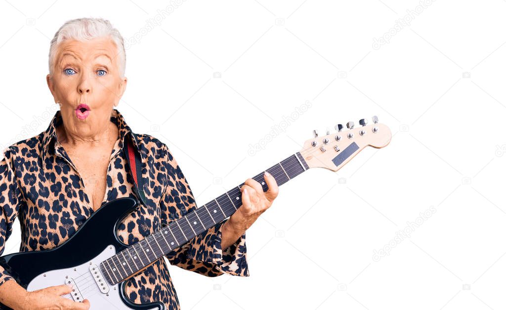 Senior beautiful woman with blue eyes and grey hair with modern look playing electric guitar scared and amazed with open mouth for surprise, disbelief face 