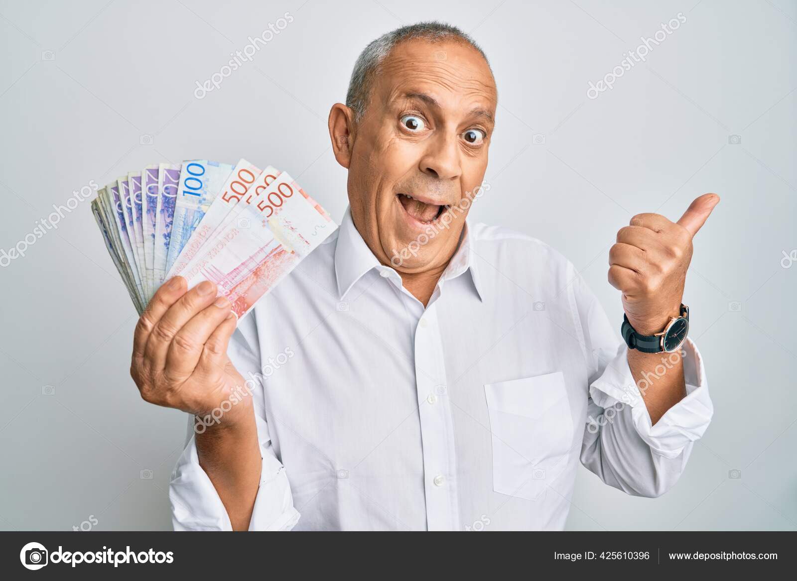 英俊的老人手握瑞典克朗钞票把大拇指指向旁边笑容满面张开嘴——图库图片© Krakenimages.com #425610396