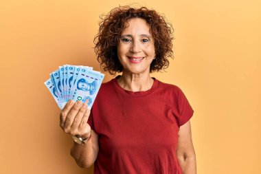 Güzel orta yaşlı bir kadın elinde 10 Yuan 'lık Çin banknotları tutuyor. Pozitif ve mutlu görünüyor. Kendine güvenen bir gülümsemeyle dişlerini gösteriyor. 